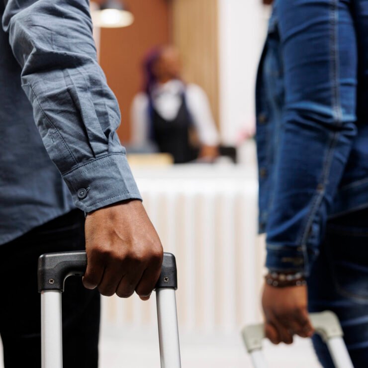 Couple pulling luggage in hotel Close up of African American couple arriving at hotel or resort, tourists standing with suitcases in lobby and waiting for check-in process. Cropped photo of man and woman pulling luggage
